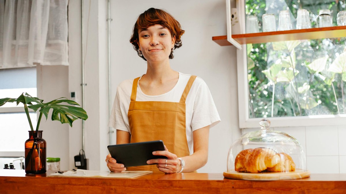 korean small business owner looking at customer data on a tablet in a cozy cafe
