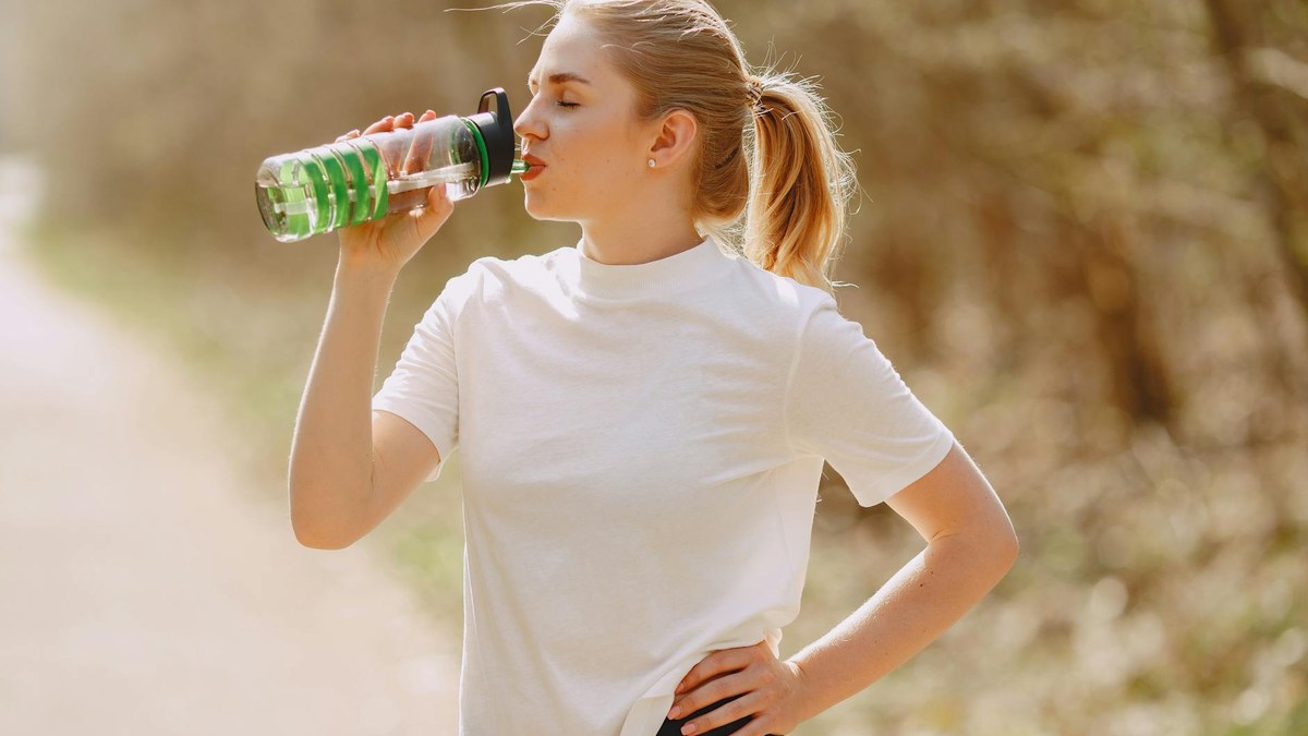 young korean woman smiling while drinking from a stylish green water bottle outdoors