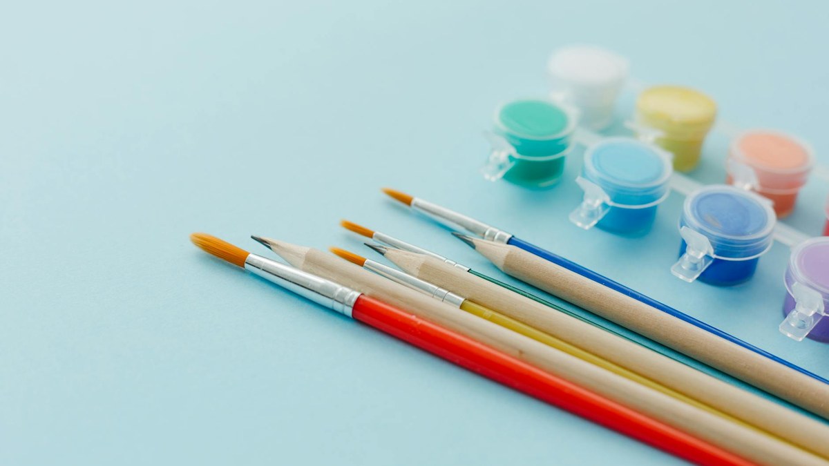 Close-up of diverse art supplies like paintbrushes, watercolor palette, and drawing pencils on a wooden table