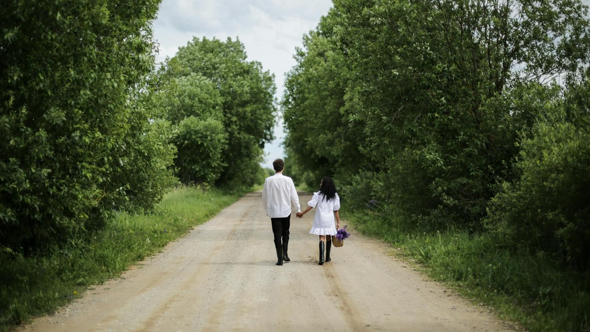 korean couple walking on a scenic path in a lush green forest with sunlight filtering through the trees