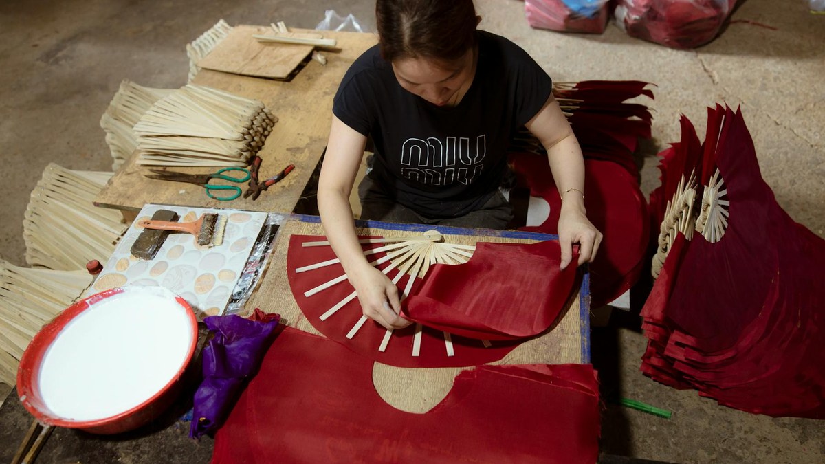 A person holding a handmade paper fan with Korean traditional patterns in a workshop
