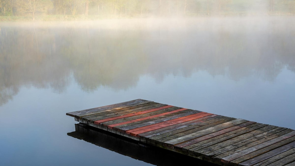wooden dock in a lake with calm water and trees reflecting