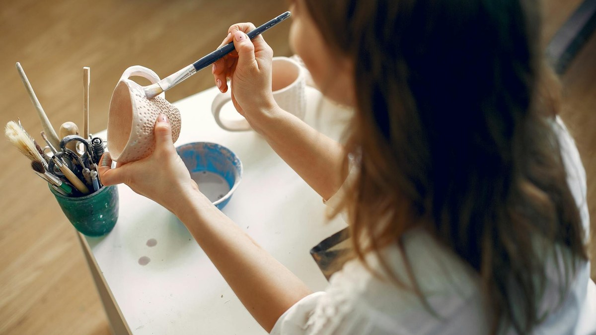 woman happily painting pottery in a bright studio