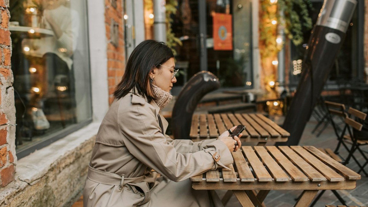woman in a cafe wearing a light blue blouse and beige wide-leg pants with a beige trench coat