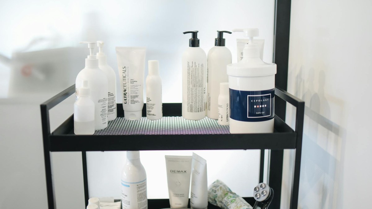A collection of skincare products arranged neatly on a minimalist white shelf, including a toner, serum, and gel moisturizer