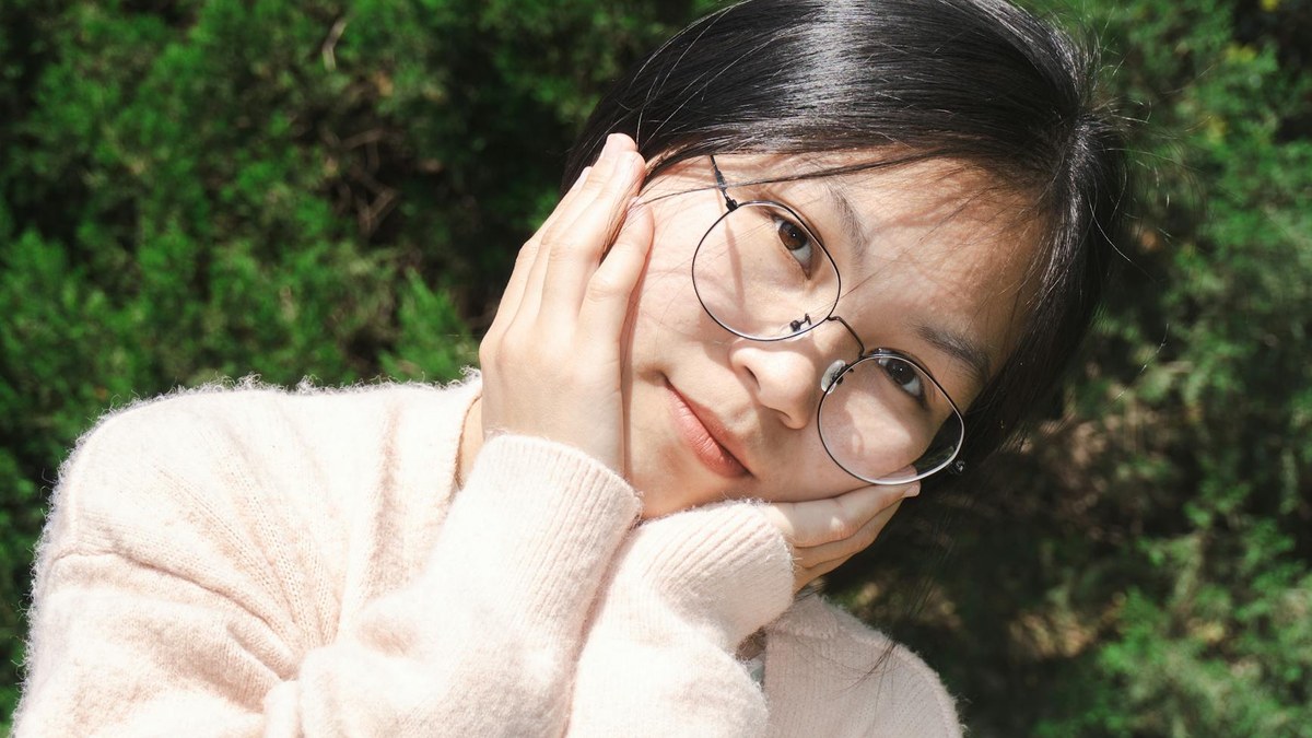 Young Korean woman with glowing, healthy skin smiling outdoors on a sunny day